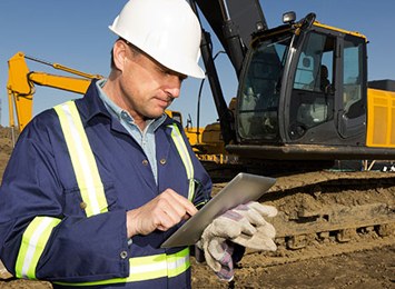 A site manager in a hard hat checking a tablet